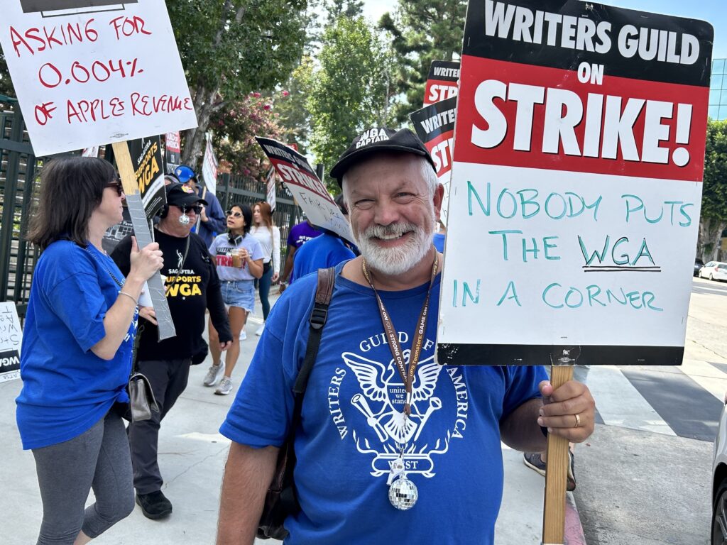 Brian Nelson has been a WGA member for 30 years. On the picket line outside CBS Radford Studios on Friday, The screenwriter said “whatever deal we make may be the template for other deals going forward.” Brian Nelson holding a sign at the picket line