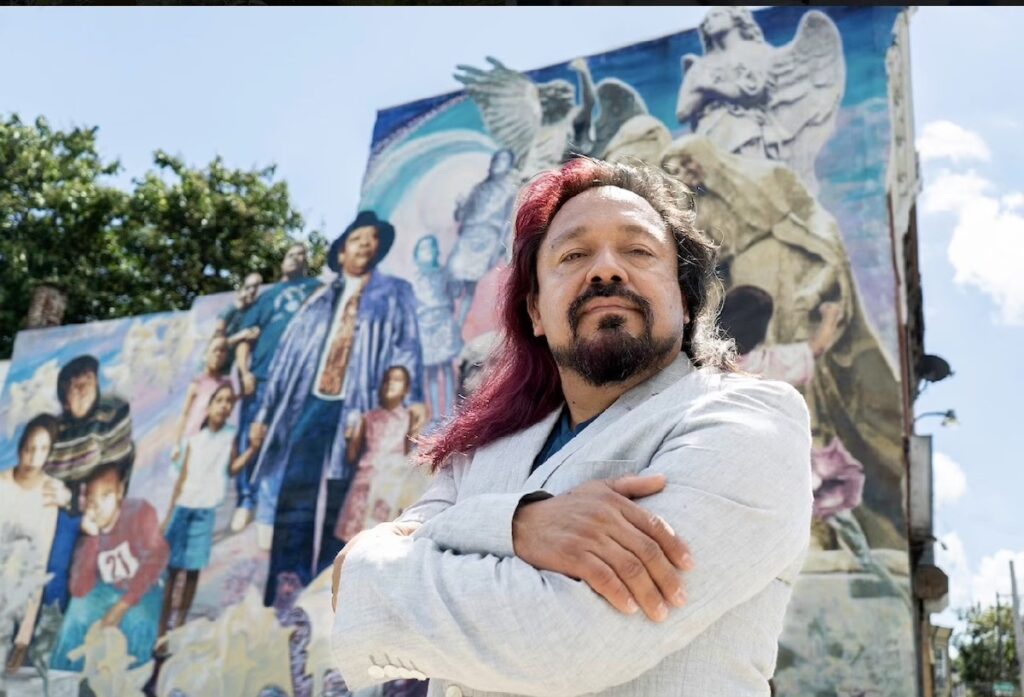 Cesar Viveros poses for a photo in front of his mural