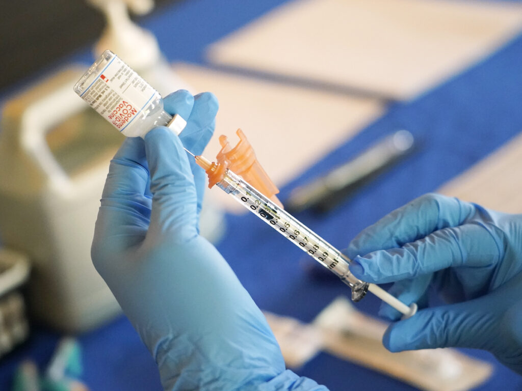 A medical professional prepares a vaccine syringe.