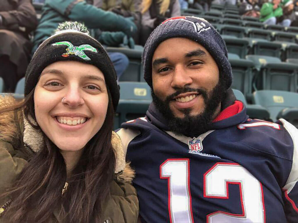 eaglesfans-herrera-husband-patriots A woman wearing a Philadelphia Eagles hat, and a man wearing a New England Patriots jersey and hat