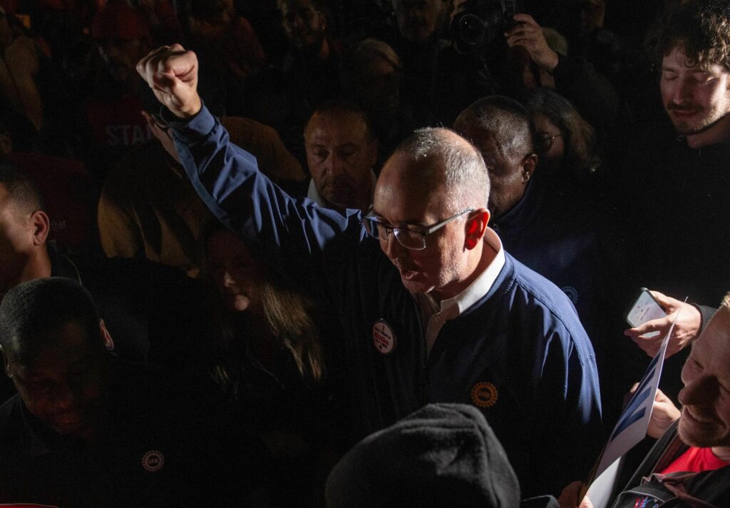 United Auto Workers President Shawn Fain speaks outside the UAW Local 900 headquarters across the street from the Ford Assembly Plant in Wayne, Mich. The union announced the start of a strike at three factories just after midnight on Friday. Shawn Fain raising his fist in a crowd of people.