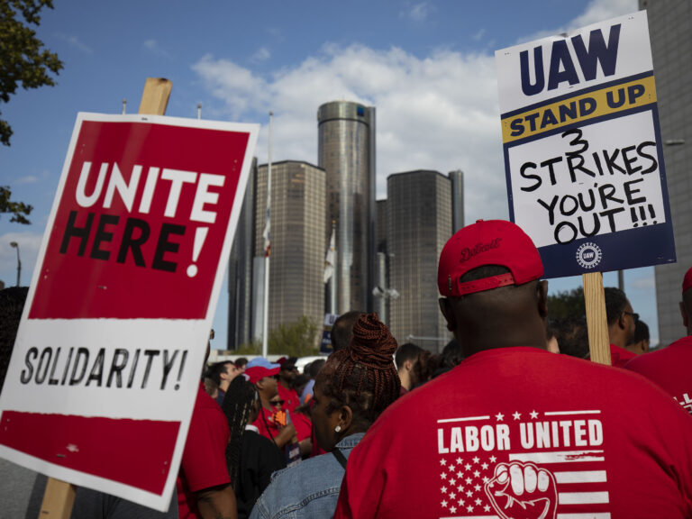 Striking auto workers hold signs.