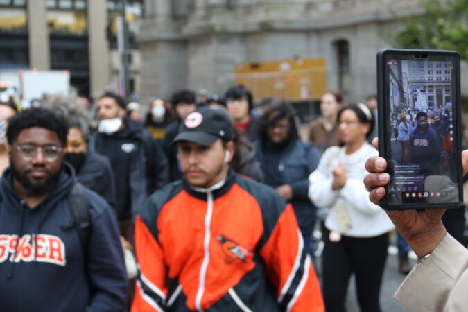 A person films protesters as they walk by.