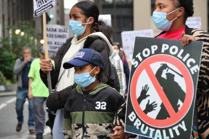 Protesters stand outside of City Hall holding a sign that reads 