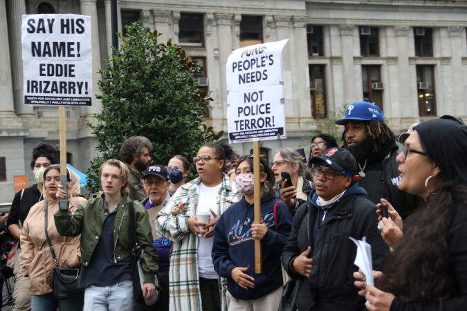 Protesters stand outside of City Hall holding signs that read 