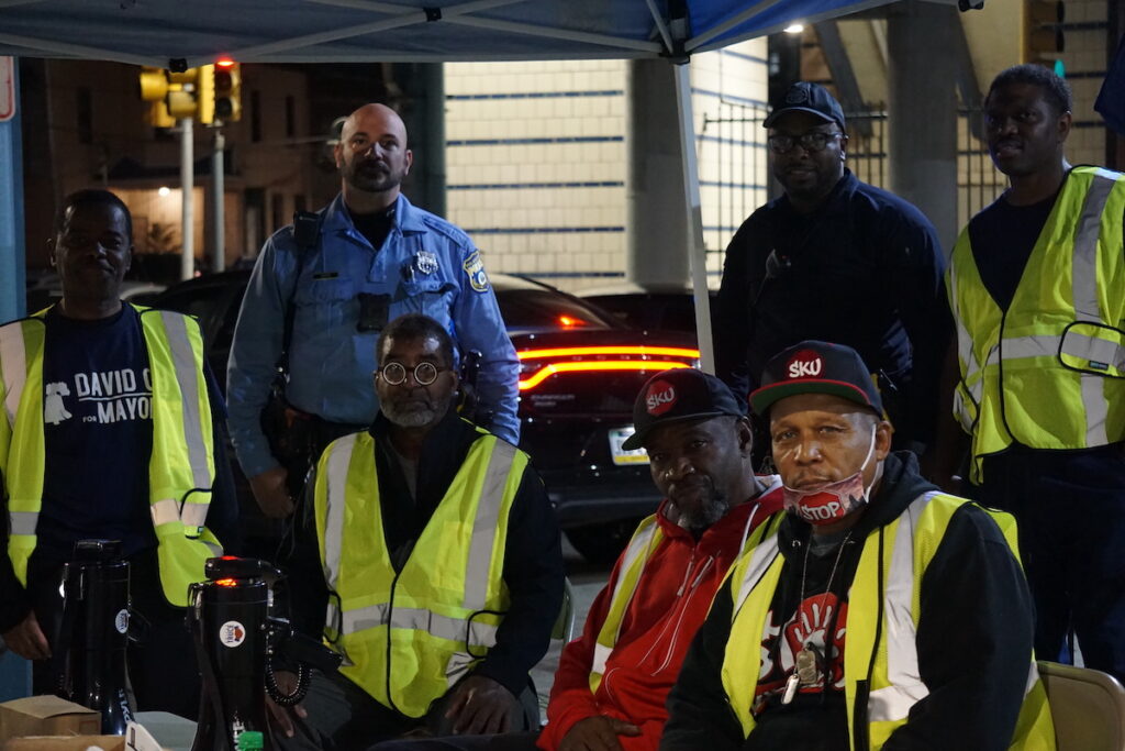 Jamal Johnson, Emmanuel Bussie, and other Operation Hug the Block volunteers sit at their base tent, across the street from Kensington's Tioga Station.