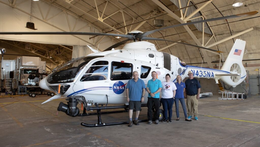 5 people posing in front of a NASA helicopter