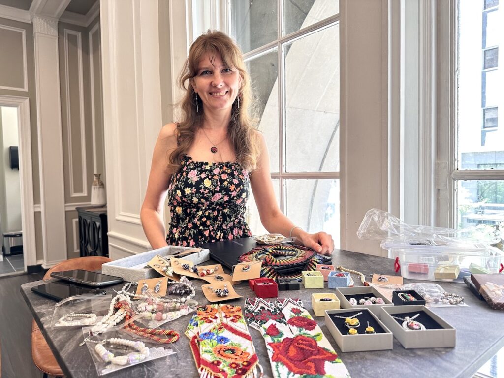 ukraine-arts-1 Oksana Pivush poses for a photo with her jewelry and other art displayed on a table in front of her.