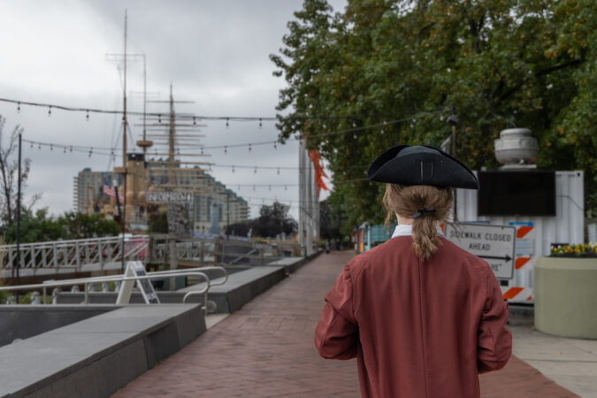 A Benjamin Franklin re-enactor seen from behind next to the waterfront.