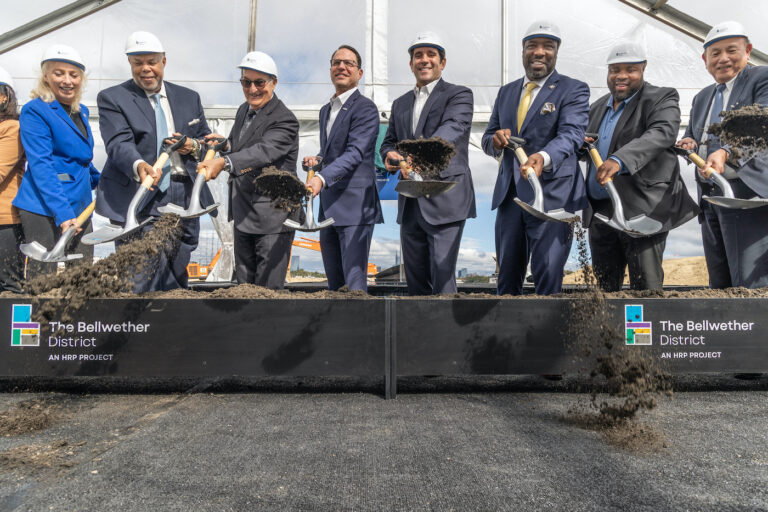 Several people in hard hats scooping dirt with shovels