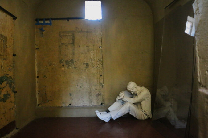 A statue of a man bent over in a corner of a former cell