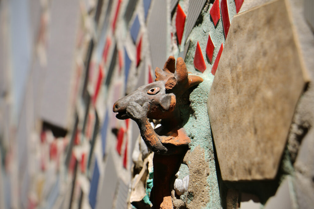 An up-close view of a sculpted creature's face on a mosaic wall.