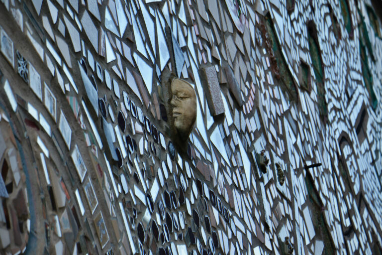 A tile bearing a double-sided face protrudes from a mosaic-ed wall.