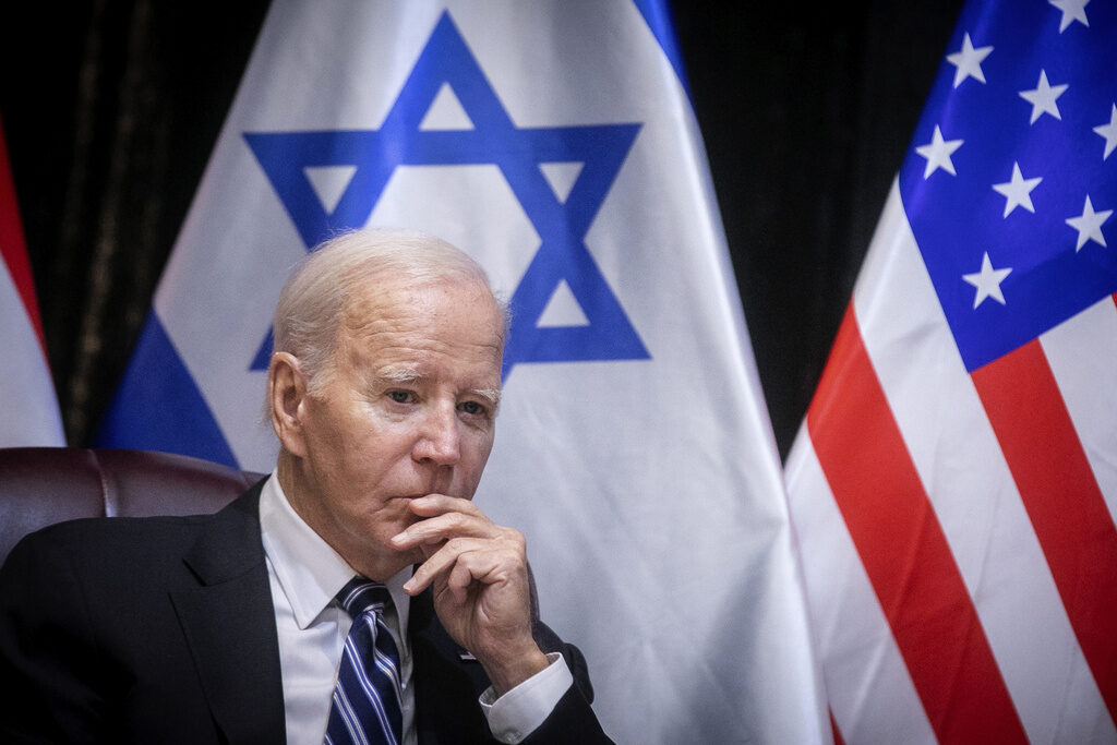 Joe Biden Biden sits in a chair, hand to face, with the Israeli and U.S. flags visible in the background.