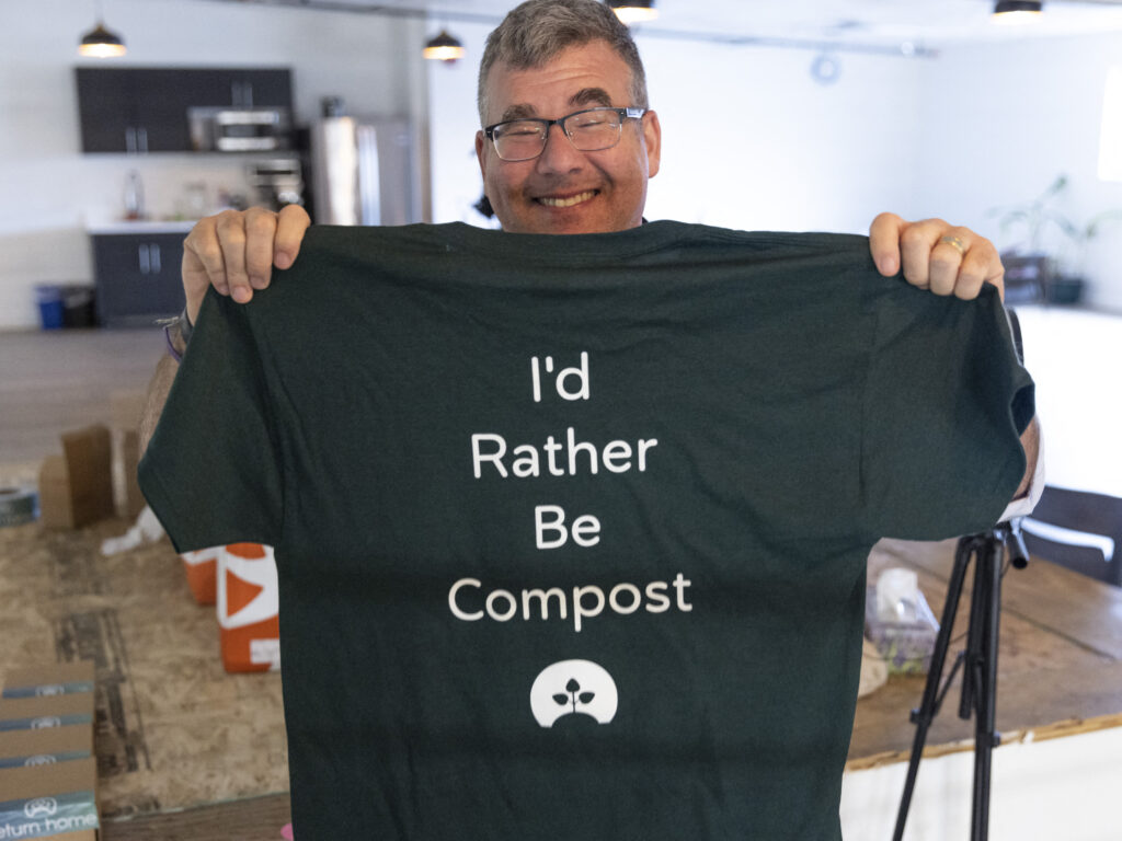 Return Home CEO Micah Truman holds up a T-shirt with a lighthearted slogan ("I'd rather be compost") during a tour of the Return Home funeral home, which specializes in human composting, in Auburn, Wash., on March 14, 2022. Washington in 2019 became the first state in the U.S. to make it a legal alternative to cremation.