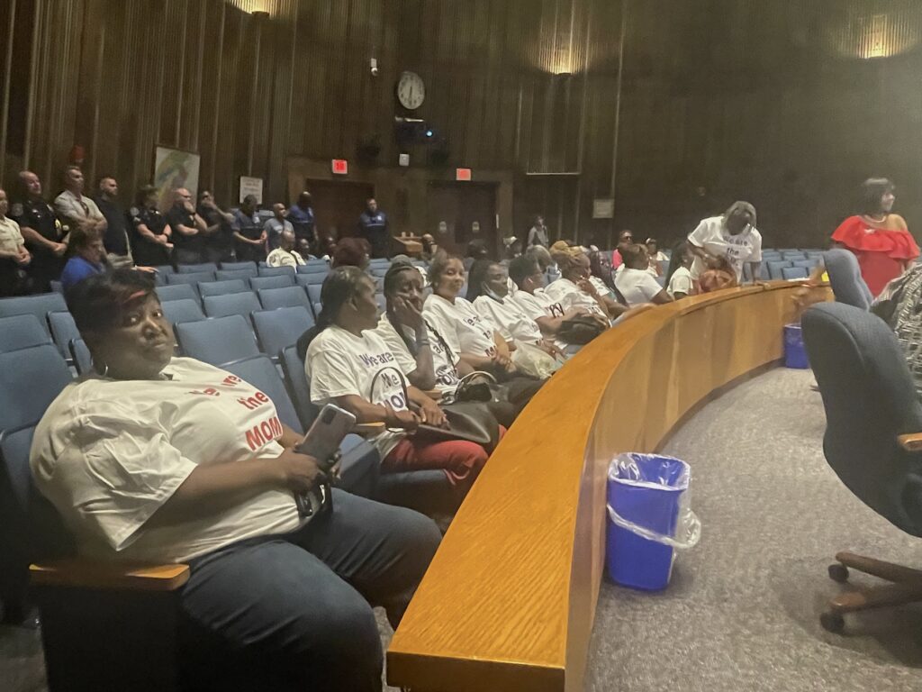 A group of women sitting in chairs at a city council hearing.