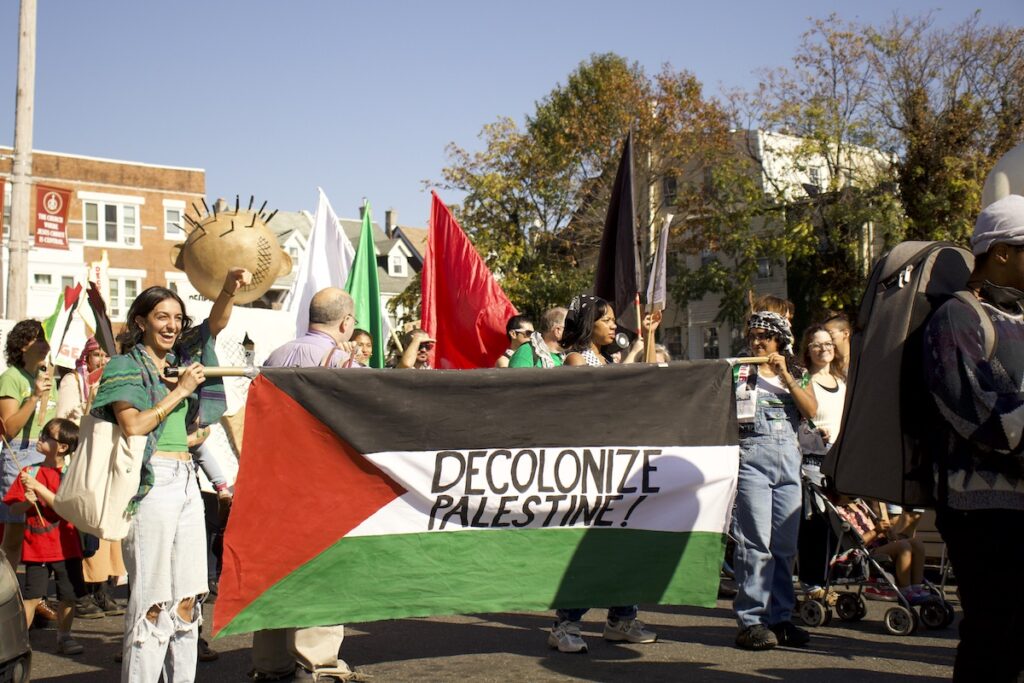 Pro-Palestine marchers hold a Palestinian flag that reads "Decolonize Palestine"