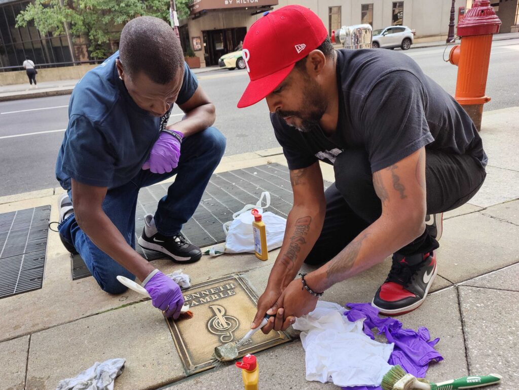 Two men scrubbing the sidewalk plaque