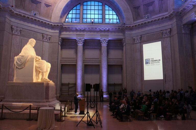 A group of people are gathered in a large room inside the Franklin Institute.
