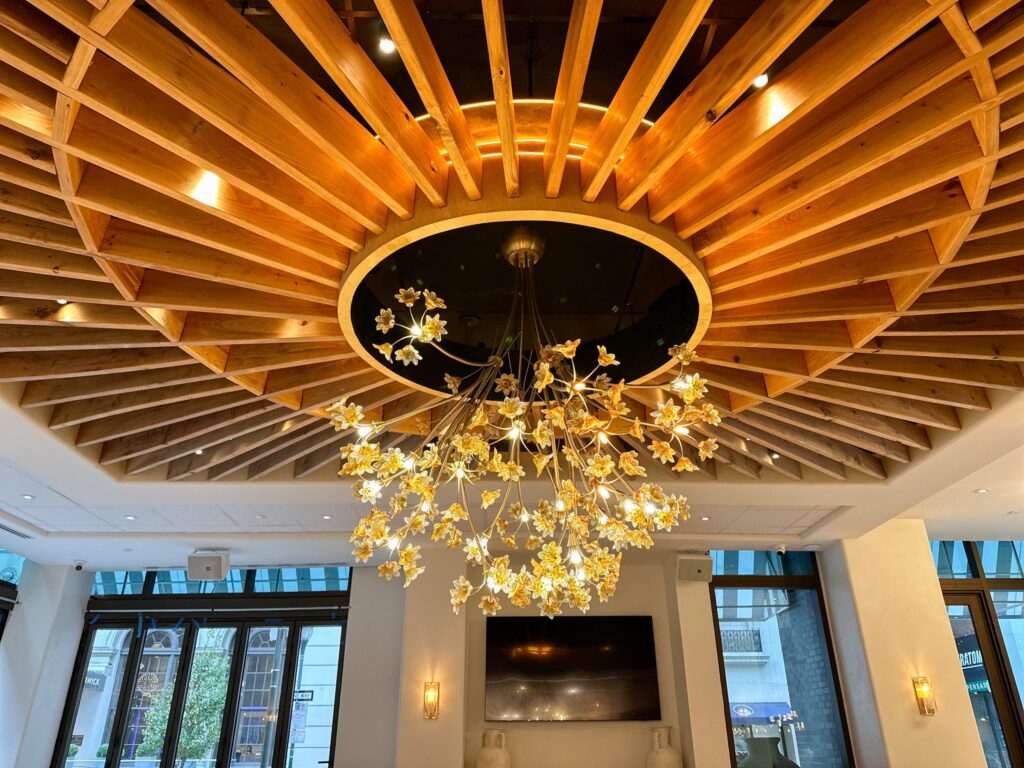 almyra-greekrestaurant-06-scaled A golden chandelier and elaborate designs are visible on the ceiling of a large room.