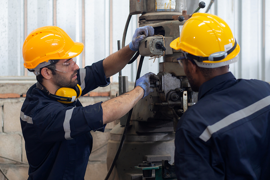 Workers wearing hard hats look at a machine