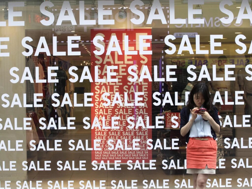 black-friday-sales-shopping A person stands in front of a window with the word Sale plastered all over it.