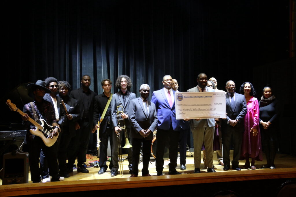 Councilmember Kenyatta Johnson holds up a check onstage surrounded by members of the Clef Club