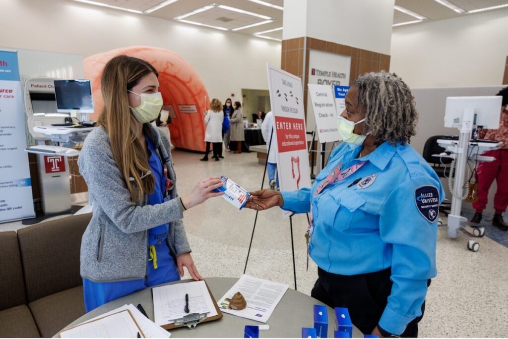 Temple medical student Julia Reed Marino gives out FIT take home kits to patients and staff in a hospital lobby.