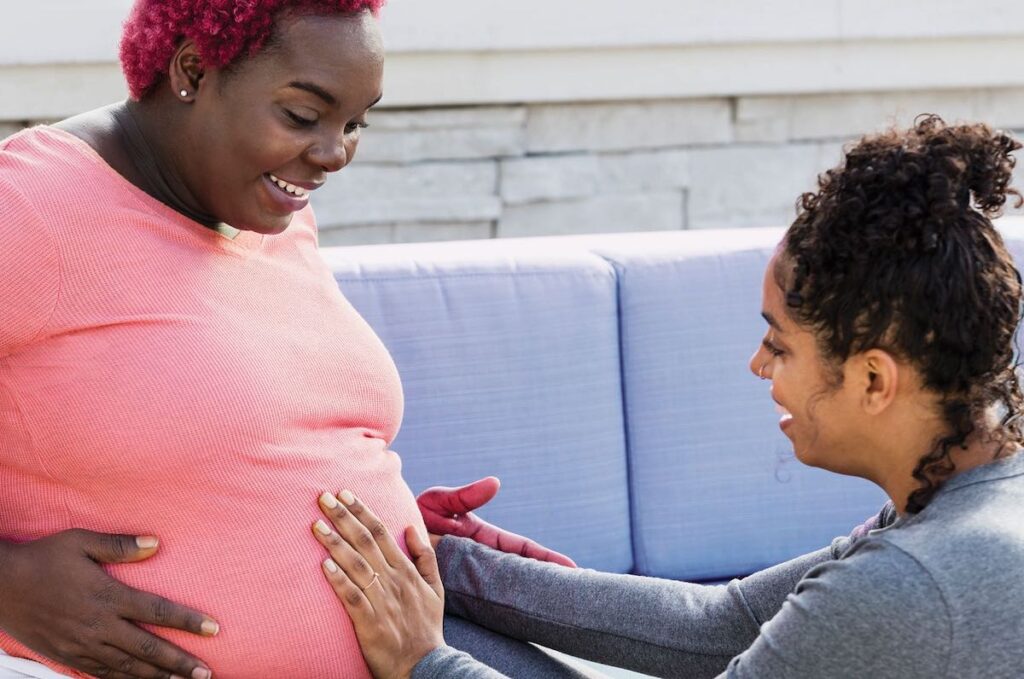 community-doula A doula places their hands on a pregnant person's stomach.