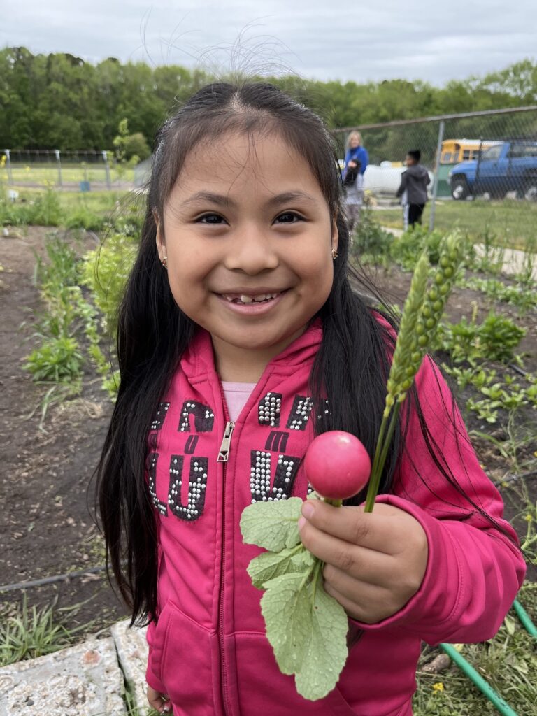 A student holds up a radish, smiling