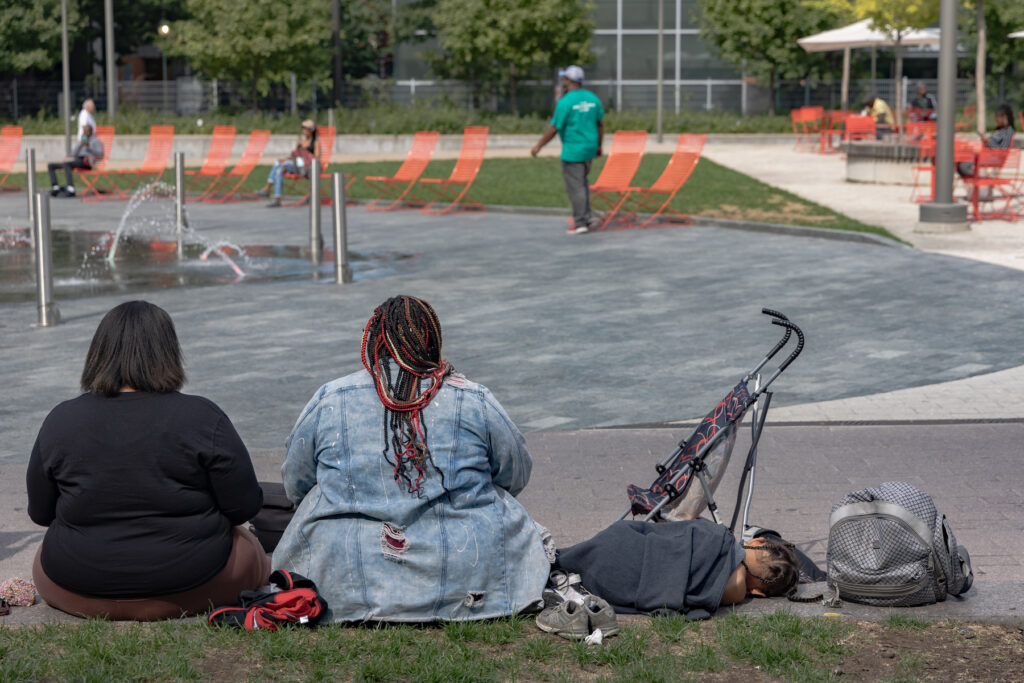 Young moms kill time at Love Park in Philadelphia. (Kimberly Paynter/WHYY) 2 woman with a young child sitting on the ground in the park.