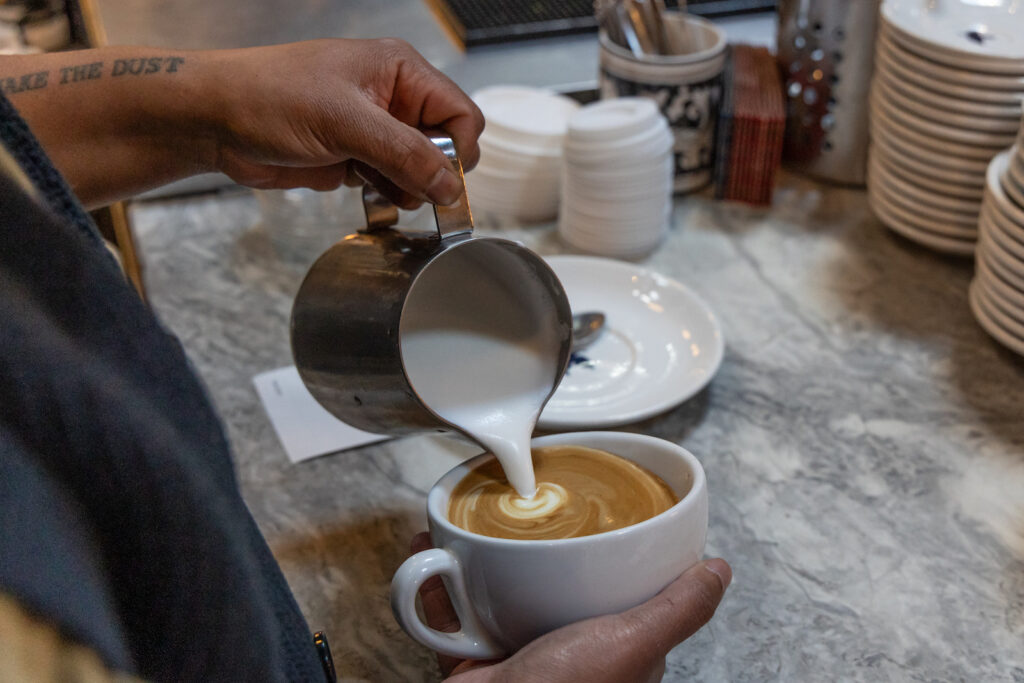 Quinn Rodriguez-Williams pours steamed milk into an espresso
