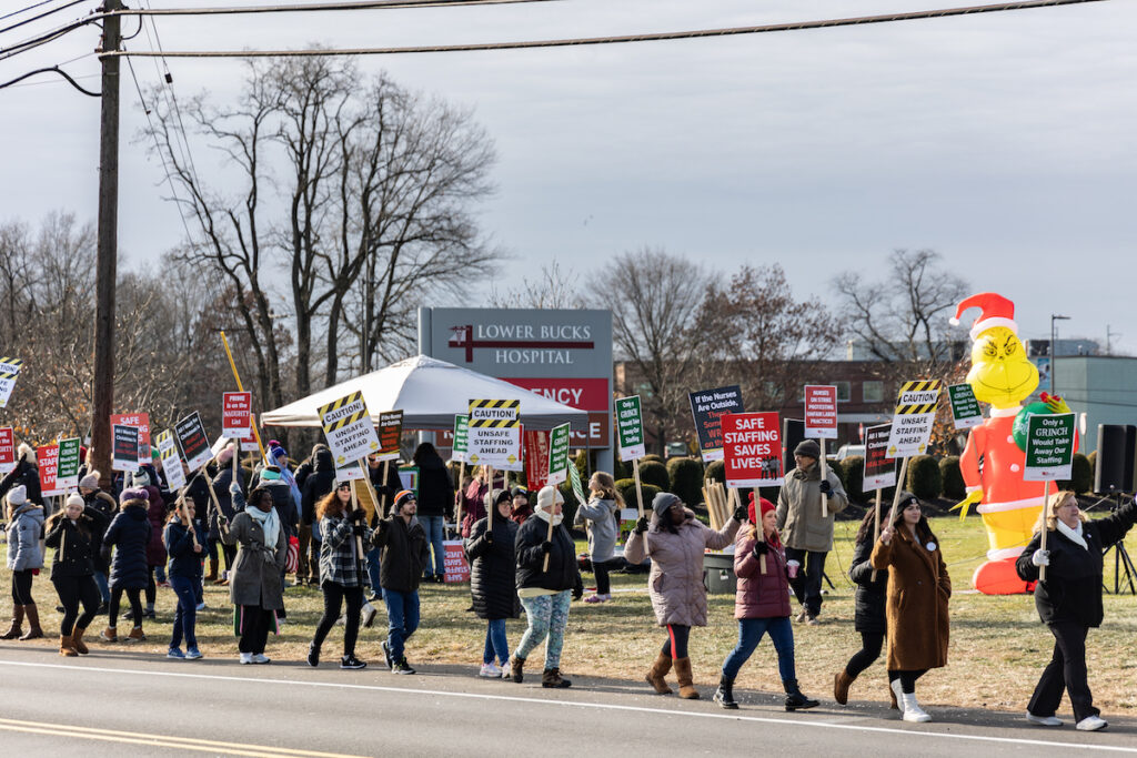 Striking nurses hold signs and walk at the picket line outside of Lower Bucks Hospital