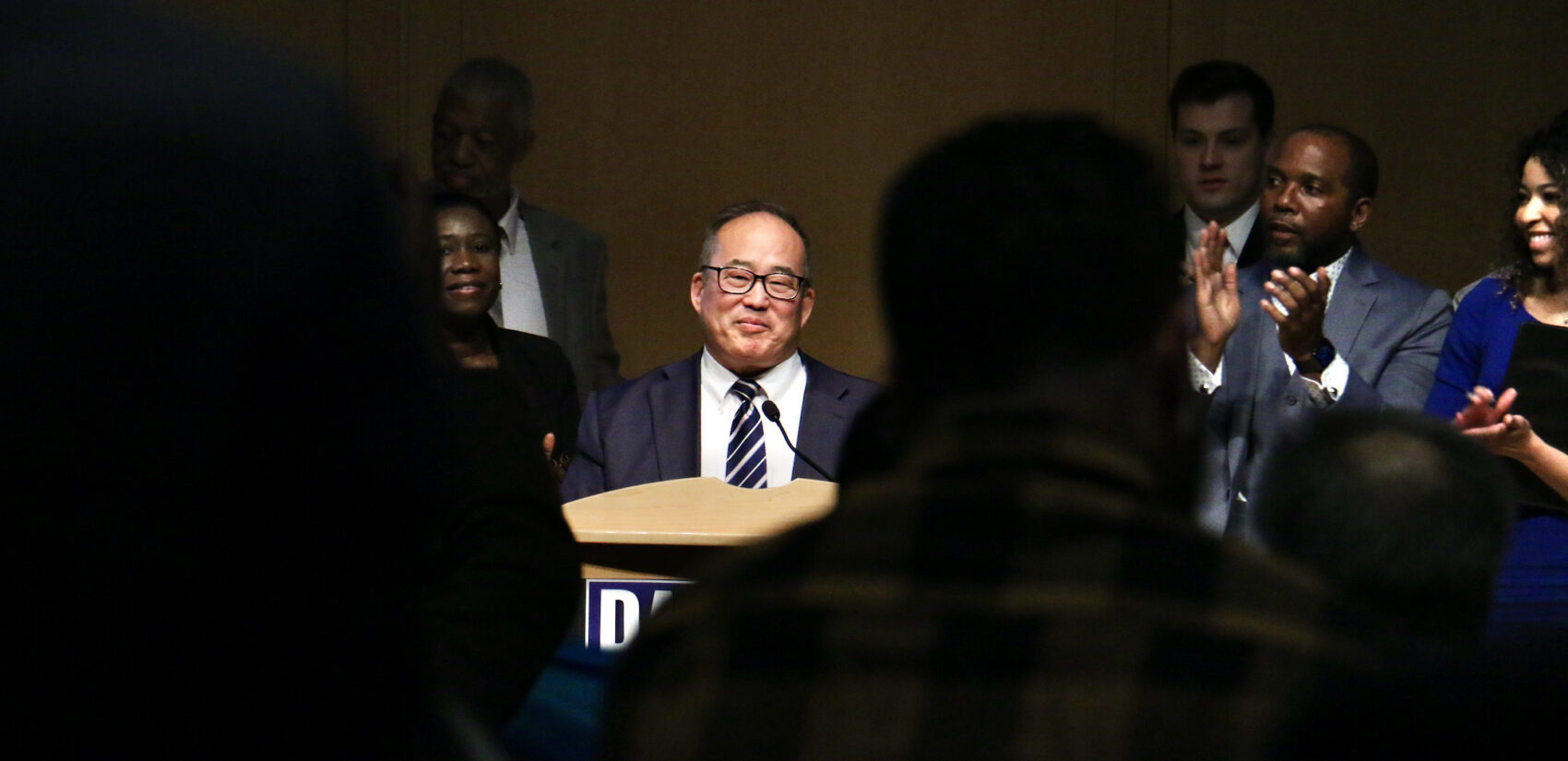 David Oh surrounded by supporters on stage.