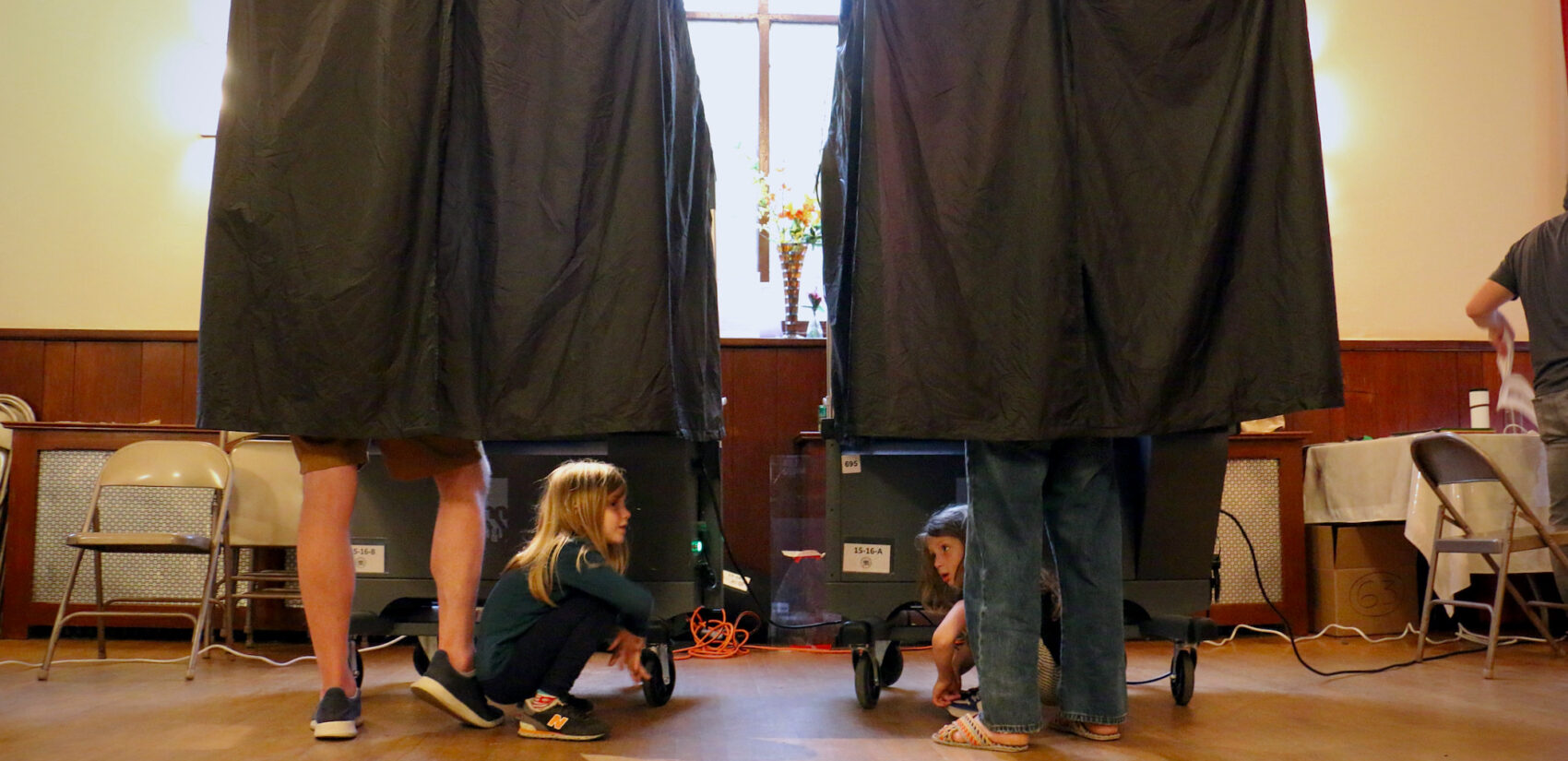 Children playing under the curtain as their parents are in voting booths.