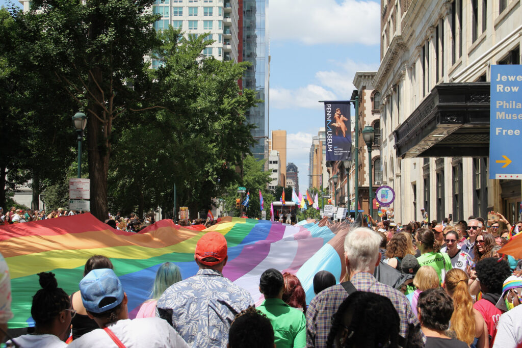 2023 06 04-c sharber-philadelphia pride march A large LGBTQ flag is carried through the streets by many people.