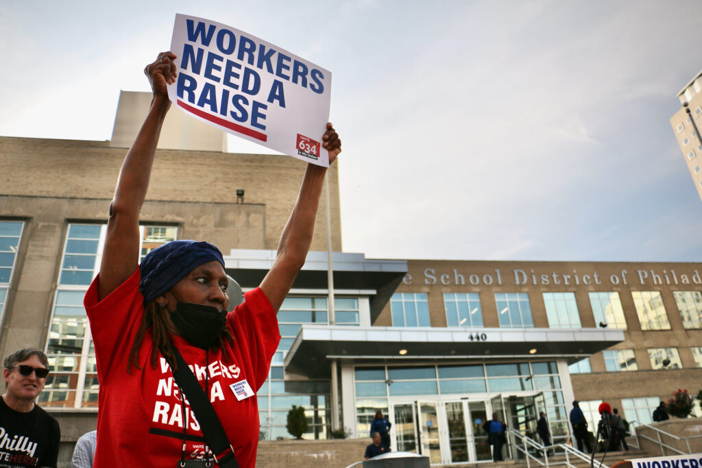 A woman holds a sign saying 'Workers need a raise'