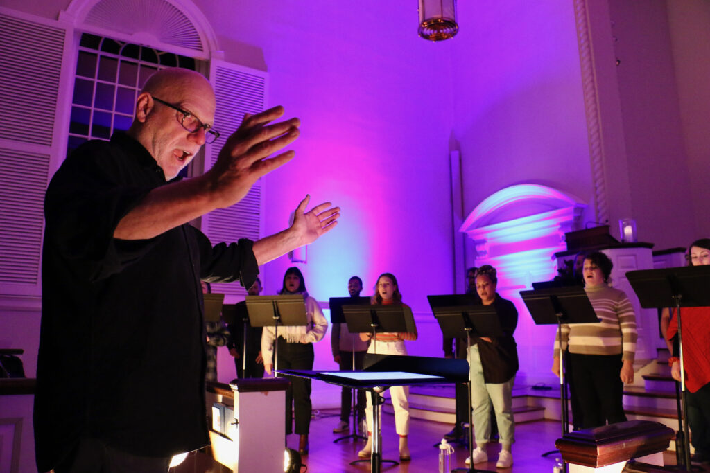 2023 12 13-e lee-donald nally-philadelphia chestnut hill presbyterian church-the crossing poor hymnal singing Donald Nally conducts in the foreground. In the background, members of The Crossing sing.