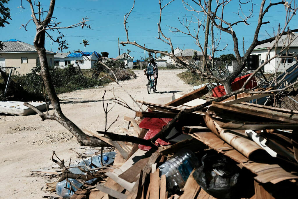 Antigua And Barbuda Struggle To Recover Months After Devastating Hurricanes A scene of damage and rubble by a dirt road as someone walks in the distance.