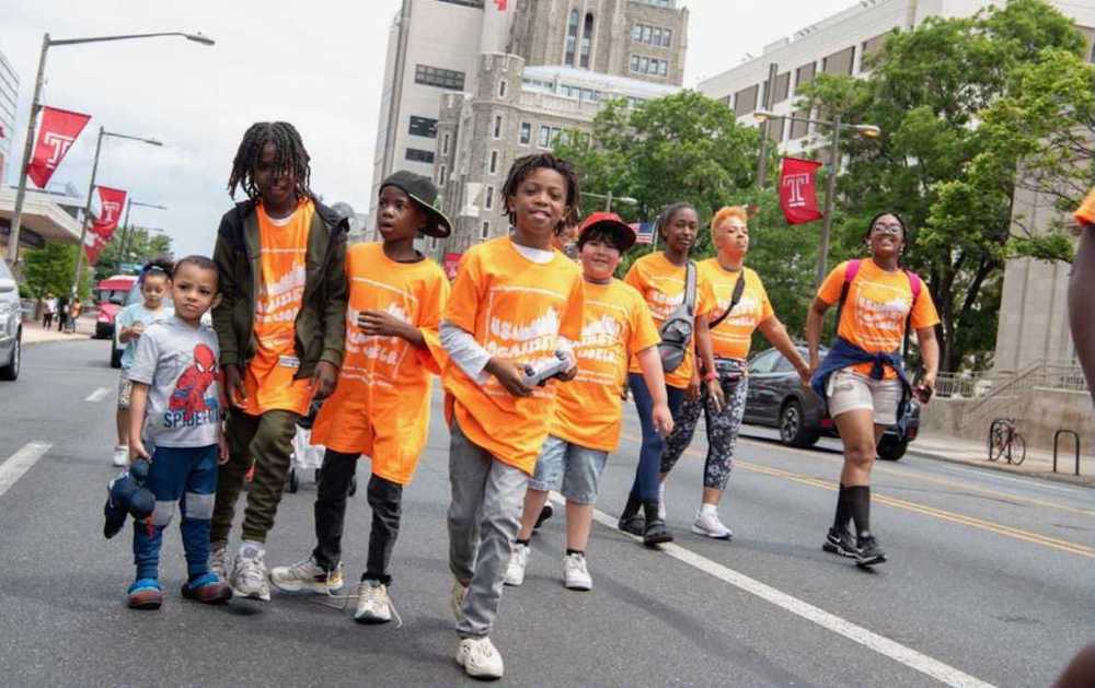 A group of kids wearing orange T-shirts participate in a unity walk, walking down Broad Street.