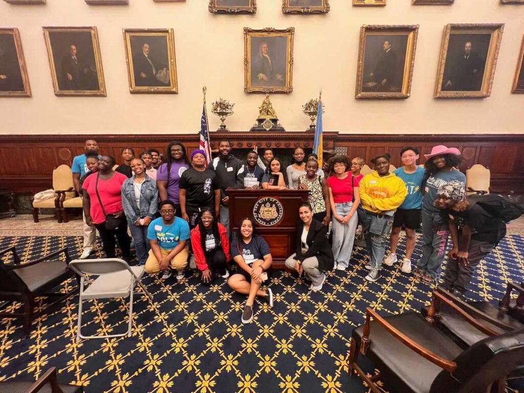 A group of people pose for a photo inside of one of the main meeting rooms of Philadelphia's City Hall