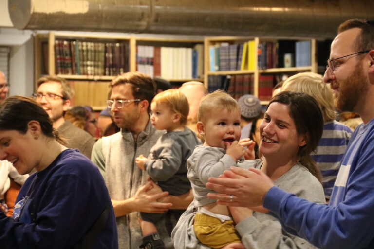 People holding children and smiling together stand in a crowd.