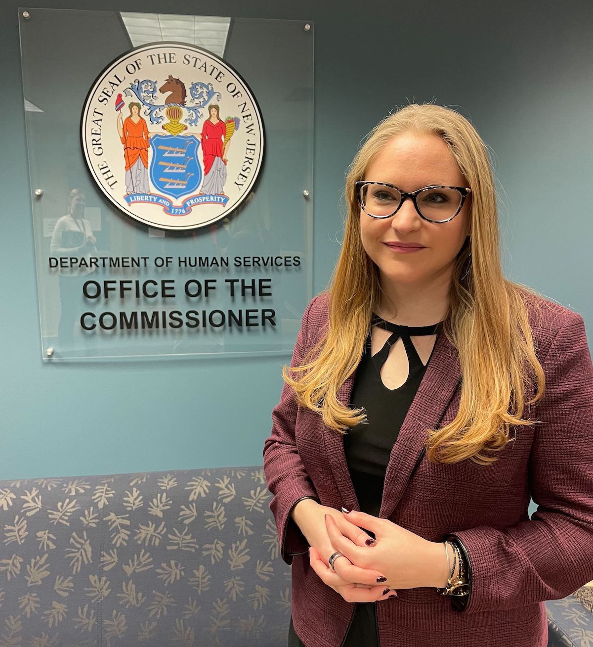 Sarah Adelman poses for a photo next to a sign that reads "Department of Human Services Office of the Commissioner"