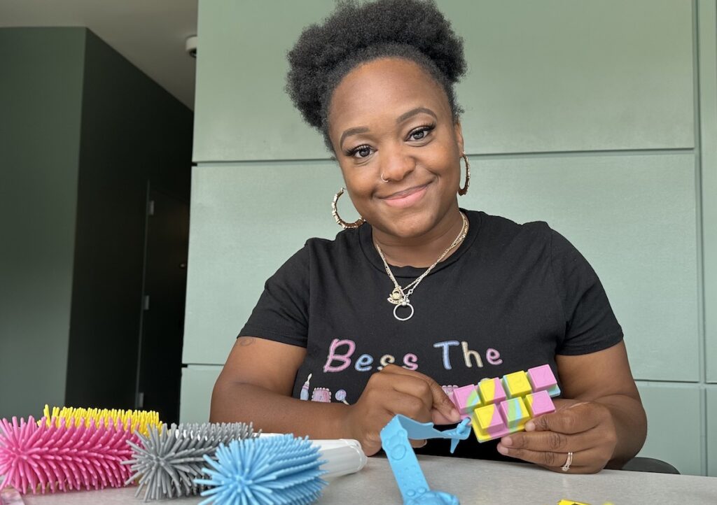 BessieLeeCappell_Philadelphia_BabyBottleBrush Bessie Lee Cappell smiles as she poses for a photo, some of her products displayed before her.