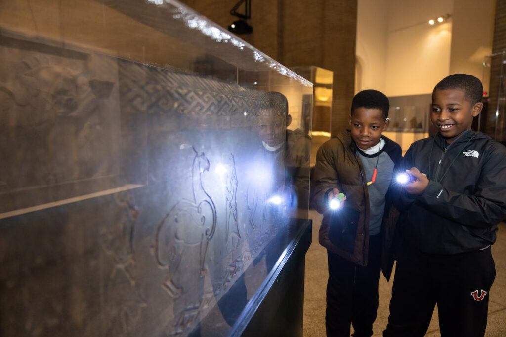 Two kids with a flashlight look at engravings on display at the Penn Museum