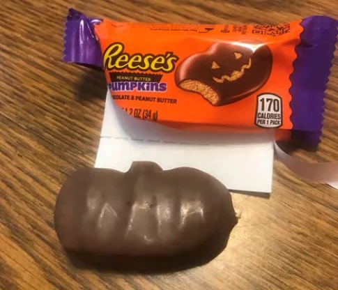 reeses-peanut-butter-pumpkins-lawsuit A Reese's Peanut Butter Pumpkin with no carved-out face next to the open wrapper with a jack-o'-lantern design.