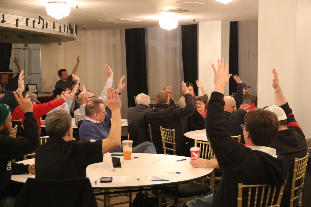People seated at tables raise their hands