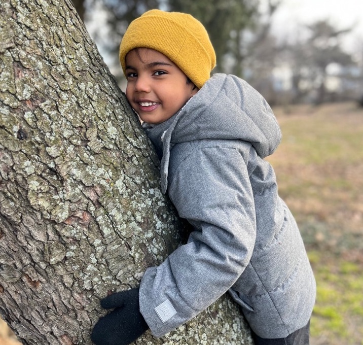 A child poses for a photo while hugging a tree.