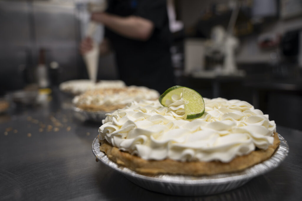 A freshly decorated Key Lime pie rests on a counter in a busy bakery kitchen at Michele's Pies, Wednesday, March 13, 2024, in Norwalk, Conn.