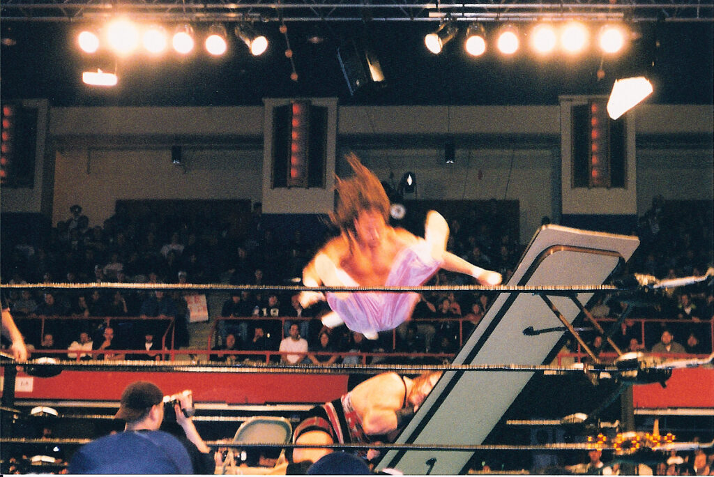 Air_Sabu_-_Rhynos_Head_About_to_go_Through_Table ECW wrestler Sabu flies through the air onto an opponent and a table as part of the promotion's hardcore style. (Source: Flickr Commons project, Jonathan Ice, https://commons.wikimedia.org/w/index.php?curid=5934466)